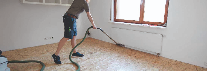 Eine Handwerkerin saugt den Boden in einem Zimmer.